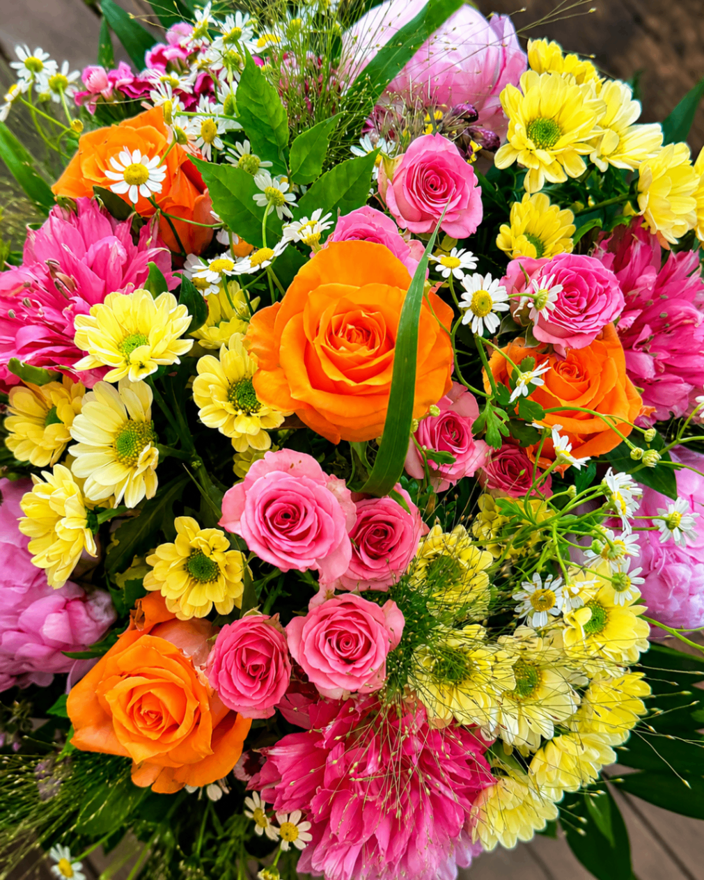 Bunter Strauß mit orangefarbenen Rosen, pinken Blüten und gelben Chrysanthemen