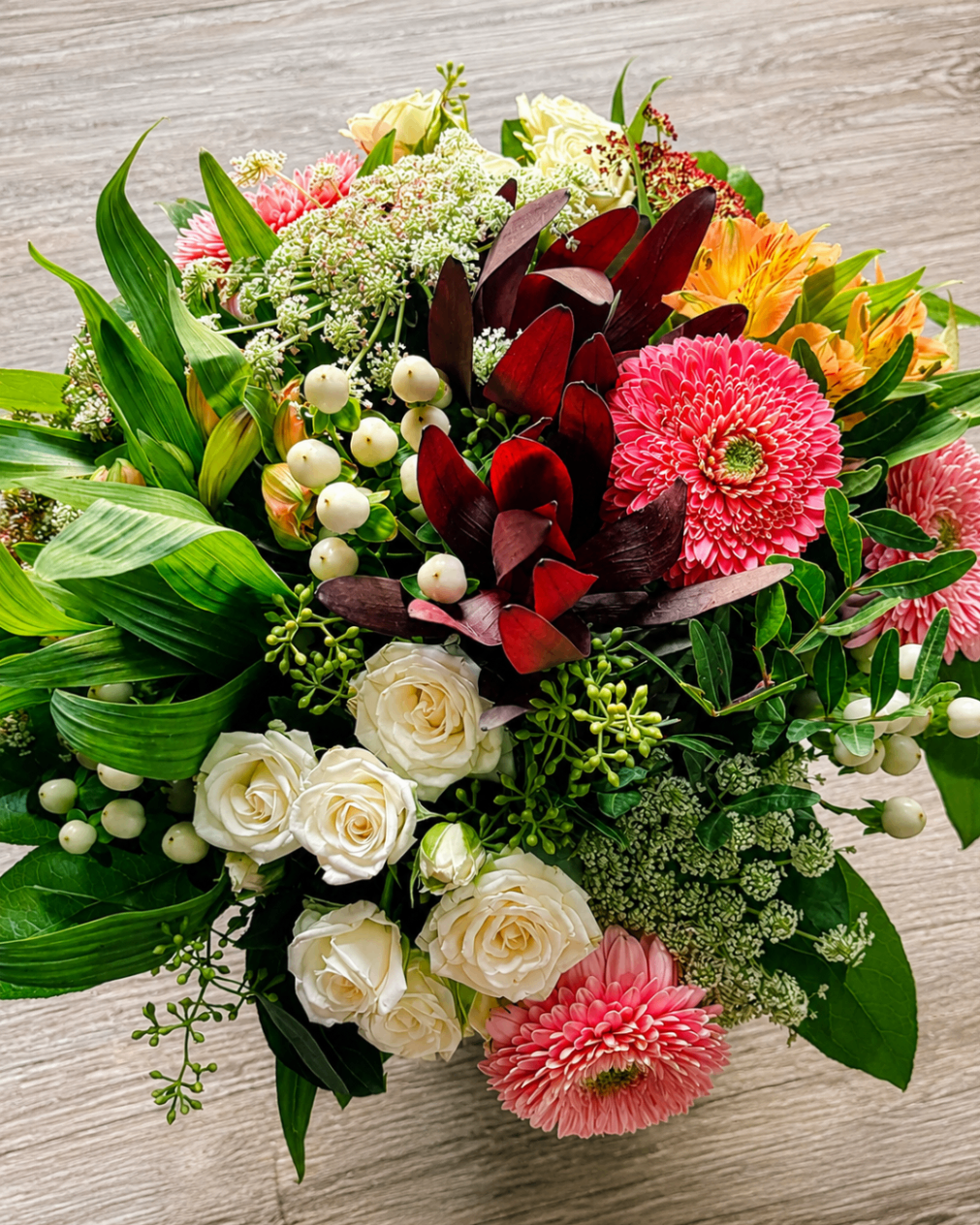 Blumenstrauß mit weißen Rosen, pinken Gerbera, Beeren und dunklem Blattwerk