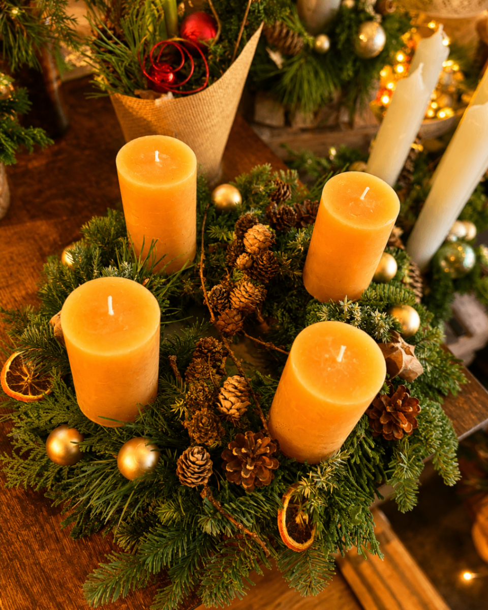 Warmer Adventskranz mit goldenen Kerzen, Zapfen und getrockneten Orangenscheiben