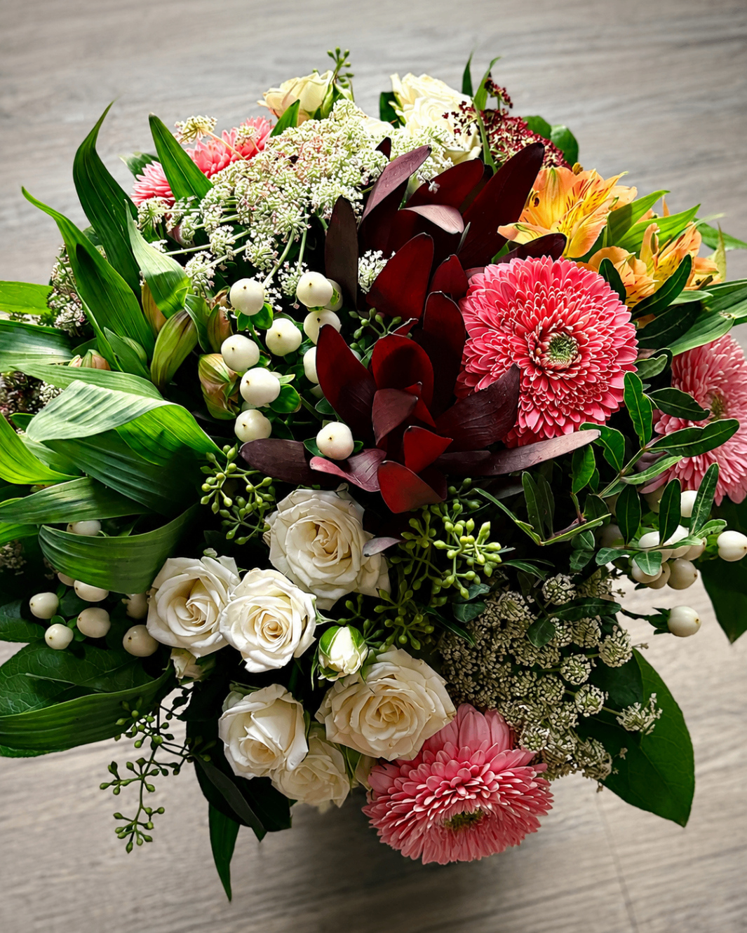Farbenfroher Strauß mit weißen Rosen, pinken Gerbera und dunklem Blattwerk