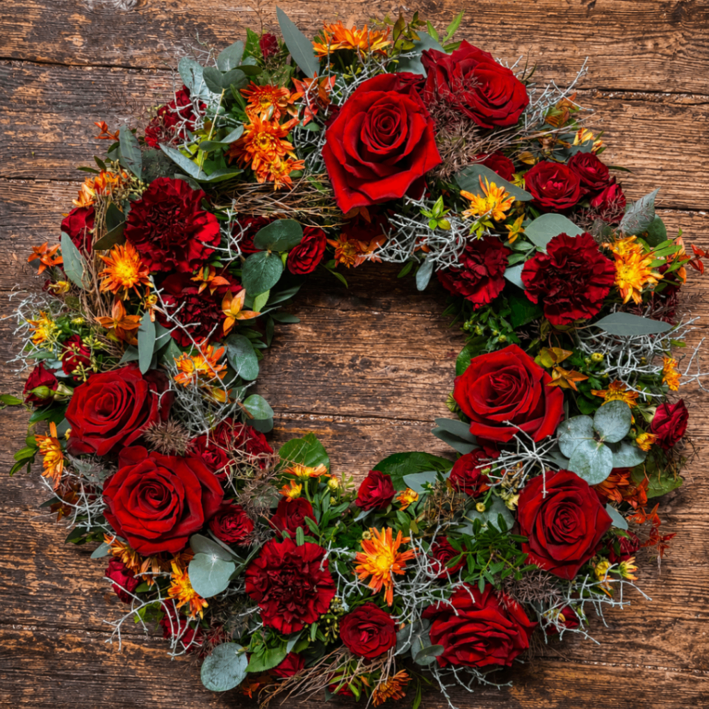 Kranz mit roten Rosen und orangefarbenen Akzenten auf Holz